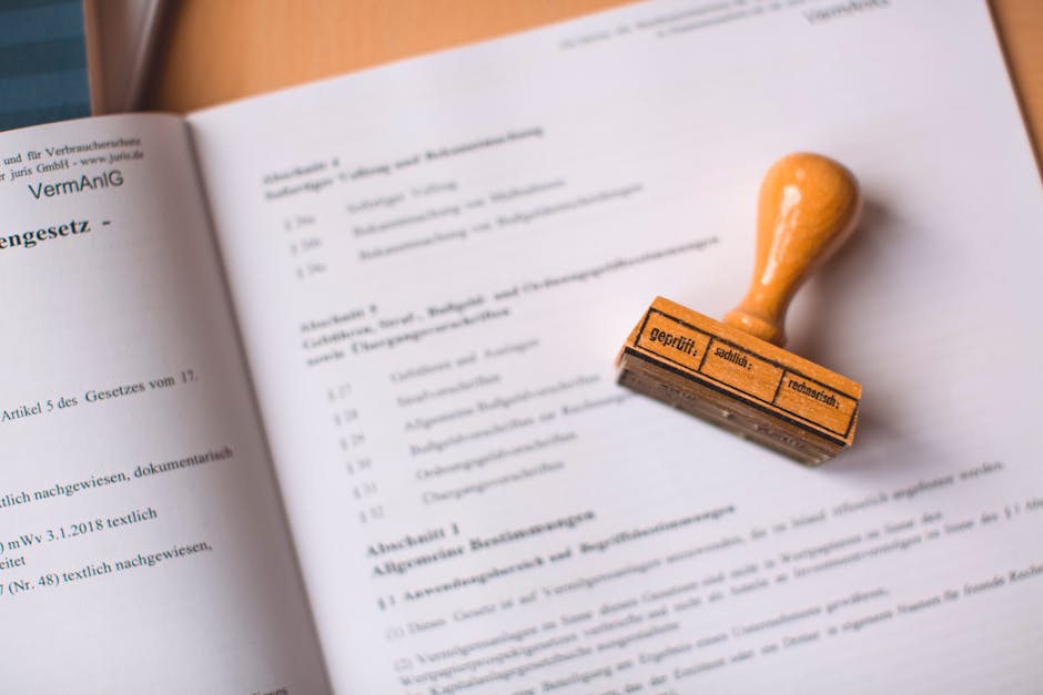 A close-up image shows a wooden stamp with an orange handle, resting on an open document printed with black text in German. The document appears to be formal, possibly legal or official paper, with some sections underlined or bolded. The stamp, positioned to the right of the page, has German words indicating it is used for verifying or legalizing documents. The scene is well-lit, with the paper lying flat on a surface, and the background out of focus to emphasize the stamp and document. This visual is relevant to house removals and moving services, as it illustrates proper documentation or legal procedures involved in home relocation, supported by professional firms such as Man and Van Mitcham during the moving process, which may include handling official paperwork or permits related to house removals as outlined in Mitcham Council permit rules.